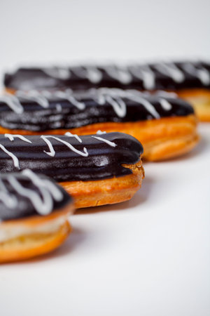 Four chocolate eclairs sit in a row on a white surface. The eclairs have chocolate frosting and...