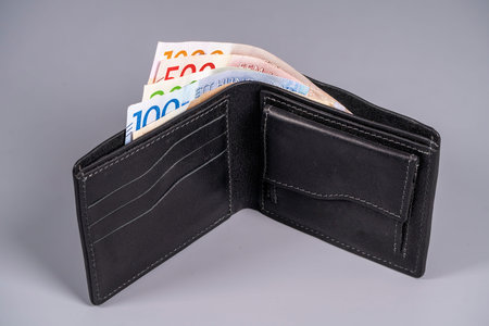 A black wallet is open, displaying several Swedish kronor notes inside. The currency shows different...