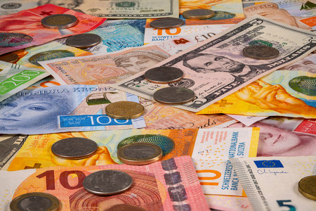 Many paper bills and coins from various countries are scattered together on a flat surface. The mix includes notes in different colors and sizes alongside various coins.の写真素材