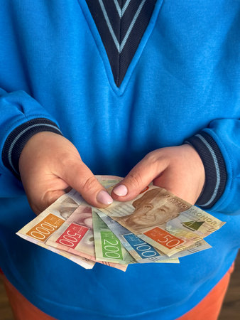 A person stands with hands slightly open, showing several Swedish kronor banknotes of different...