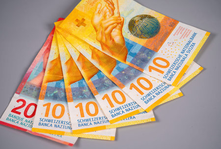 A collection of Swiss currency notes is laid out in a fan shape on a gray surface. The notes show...
