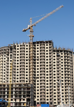 Construction crane on a background of high-rise buildings and blue sky close-upの写真素材