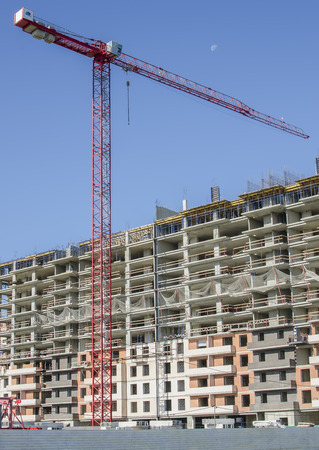 High-altitude crane on a background of monolith-brick house and blue sky.の写真素材