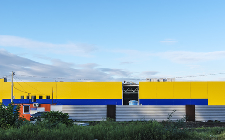 Building under construction of the yellow and blue panels behind metal fence in a field.のeditorial素材
