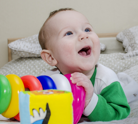Baby toddlers surrounded by toys lying on the bed, laughing and looking up. Close-up.の写真素材