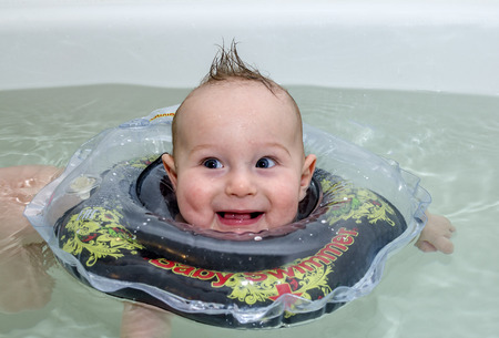 Child with rubber ring floating in a bath of clear water and smilingの写真素材