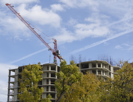 Single building crane against the blue cloudy sky, green trees and building under constructionの写真素材