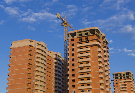 Three new brown brick buildings and a construction crane against a blue sky.の写真素材