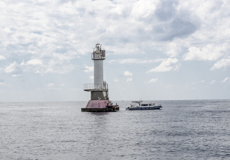 Tower lighthouse and boat against the backdrop of the sea and the overcast sky.の写真素材