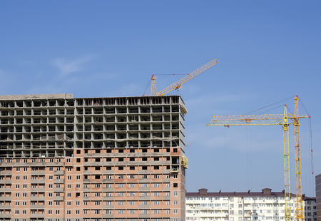 Three construction cranes among buildings under construction against the background of the blue sky.の写真素材