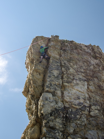 The climber ascends along a vertical limestone rock with a safety line against the blue sky.の写真素材