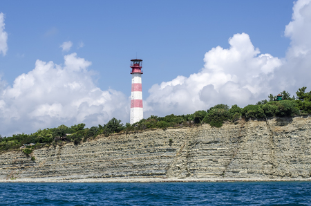 White with a red strip lighthouse tower located at the edge of the sea shore.の写真素材