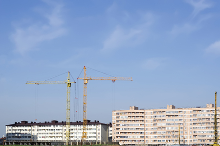 Two construction cranes against the background of the urban area and the sky.の写真素材