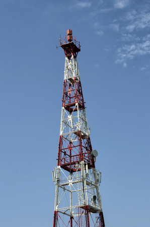 Red and white communication mast against a blue sky.の写真素材