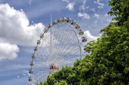 "Ferris wheel" against a cloudy blue sky and green trees on the rightの写真素材