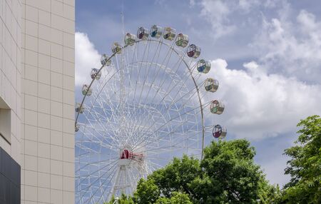 "Ferris wheel" in a city park against the blue sky and the wall of the buildingの写真素材