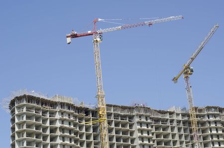 Two construction cranes tower above a large high-rise building.の写真素材