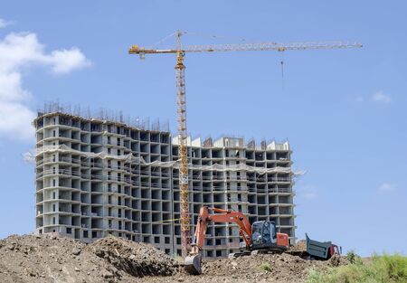 House under construction and high-rise crane. In the foreground, loading the soil with an excavator in a dump truck.の写真素材