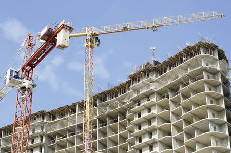 Red and yellow construction cranes over a house under construction close up.の写真素材