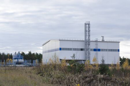 A white industrial building with associated tanks located among coniferous forests.の写真素材