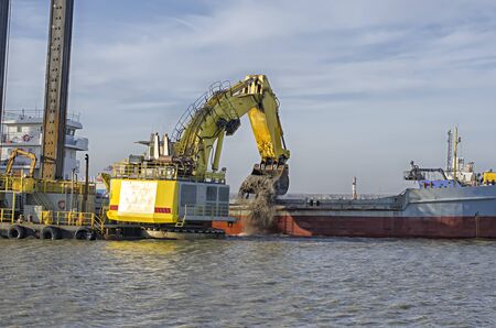 Cleaning the bottom of the port. A large yellow floating excavator loads the barge with bottom soil.の写真素材