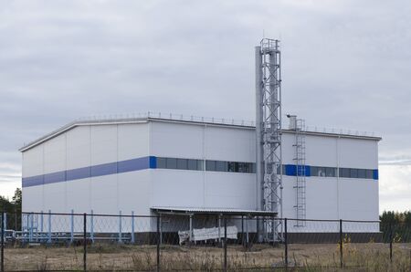 Industrial building with two metal pipes and a staircase inside a fenced area.の写真素材