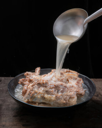 pouring milk on meat in black bowl on wooden tableの写真素材