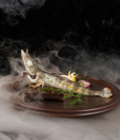 Fried fish on a wooden plate with smoke on a black backgroundの写真素材
