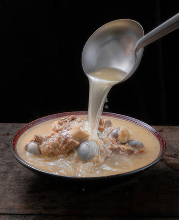 Pouring coconut milk into a bowl of soupの写真素材