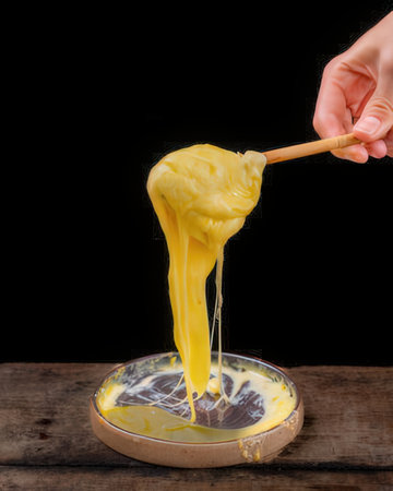 Yellow liquid dripping from a wooden spoon into a bowl on a black backgroundの写真素材