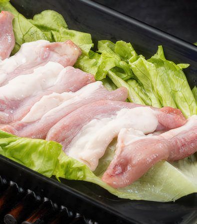 Raw pork in a black plastic container on wooden tableの写真素材