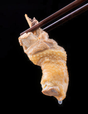 chopsticks holding a piece of raw chicken on a black backgroundの写真素材