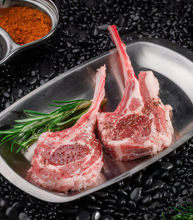 Raw lamb chops on black pebbles with rosemary and spicesの写真素材