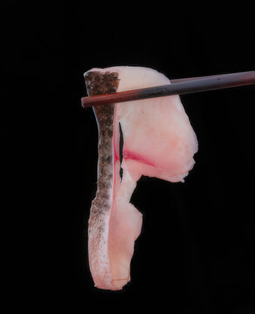 Piece of raw pork on chopsticks isolated on black background.の写真素材