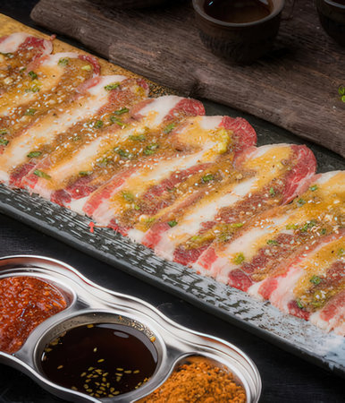 Raw beef with sauce and sesame seeds on a cutting board.の写真素材