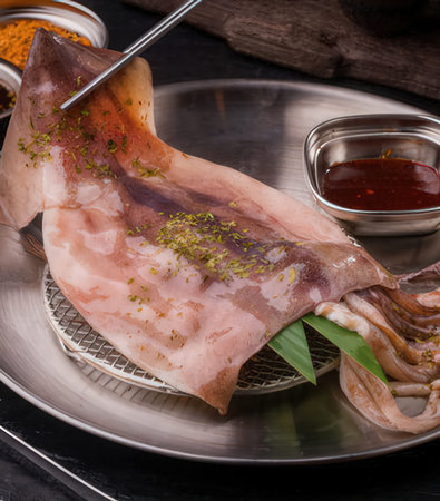 Slices of squid with spices and herbs on a metal plate