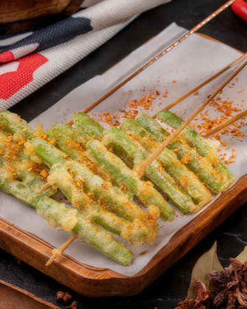 Grilled green beans on a wooden plate with chopsticks on a black backgroundの写真素材