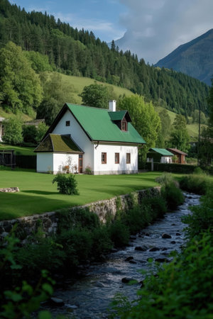 Mountain landscape with a green meadow and a small house.の素材