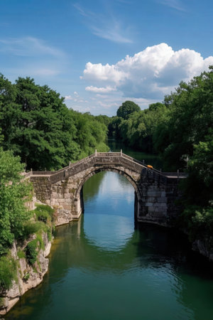 Old stone bridge over the river with green trees and blue sky.の素材
