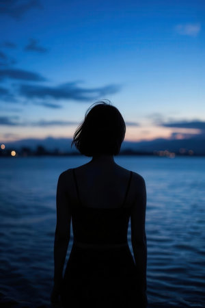 Silhouette of a young woman standing in the water at sunsetの素材