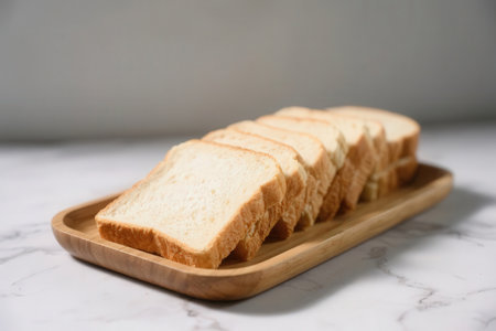 Sliced toast bread on wooden plate and white marble background.の素材