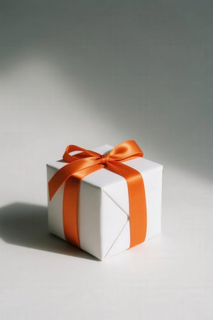 White gift box with orange ribbon and bow on a white background.の素材