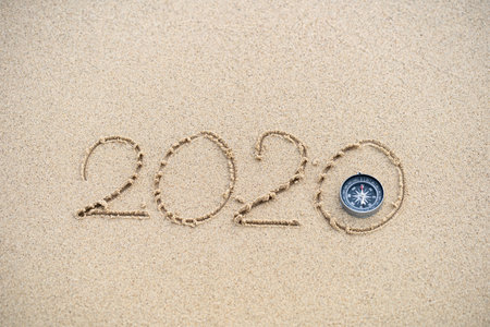 Compass and 2020 message written in the sand at the beach background. concept for vision 2020.