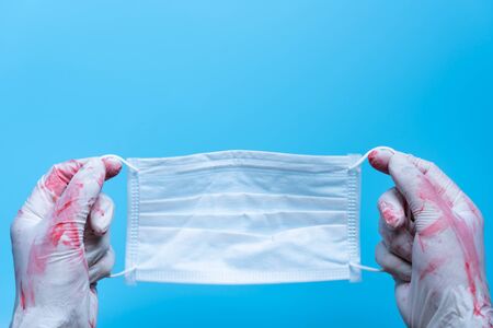 Close up doctor holds surgical mask with blood stain on blue background. Used surgical masks for protection against viruses(covid-19), Pandemic coronavirus, insurance, airborne diseases.の写真素材