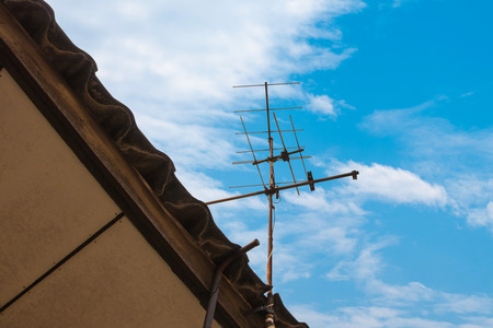 Old TV antenna on the roof with blue sky and white cloudの写真素材