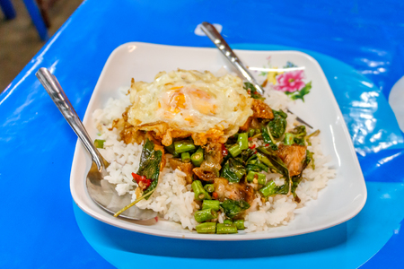 Steamed rice topped with stir-fried crisp pork , basil and over hard fried eggの写真素材