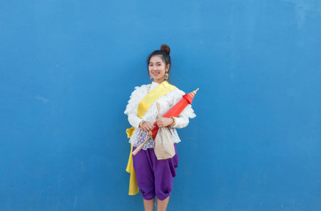 Beautiful asian woman wearing tradition thai dress with umbrella on blue wall background