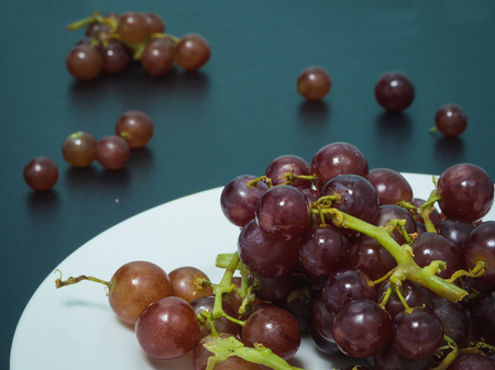 Purple grapes on white plate on the black tableの写真素材