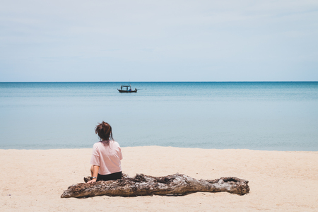 A woman sitting timber and looking at the fishing boat in the seaの写真素材