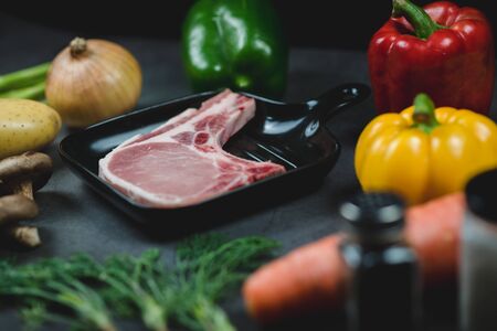 Side view of raw pork for prepare steak surrounded by organic vegetable ingredients.の写真素材